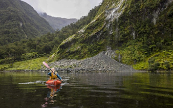 Kayaker on Doubtful Sound fjord with lush cliffs, Te Anau overnight tour.