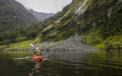 Kayaker on Doubtful Sound fjord with lush cliffs, Te Anau overnight tour.