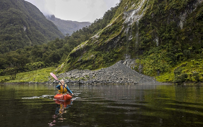 Kayaker on Doubtful Sound fjord with lush cliffs, Te Anau overnight tour.
