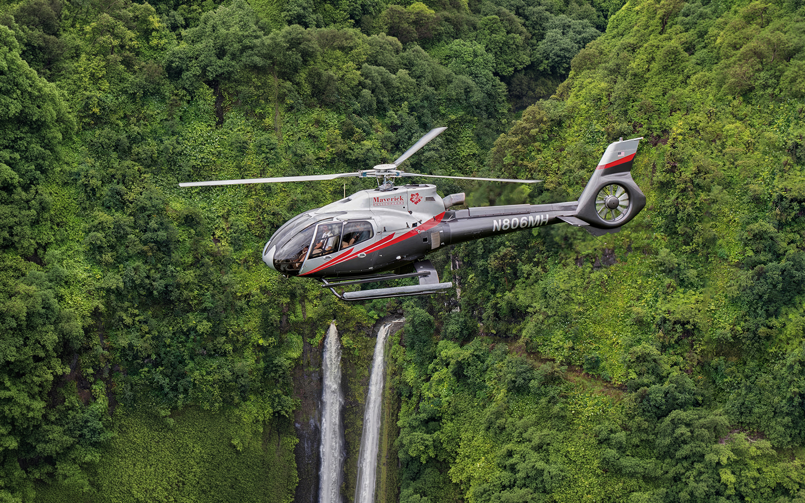 Helicopter flying over lush Hana rainforest with waterfall, Hawaii.