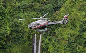 Helicopter flying over lush Hana rainforest with waterfall, Hawaii.