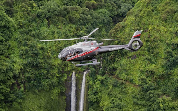 Helicopter flying over lush Hana rainforest with waterfall, Hawaii.