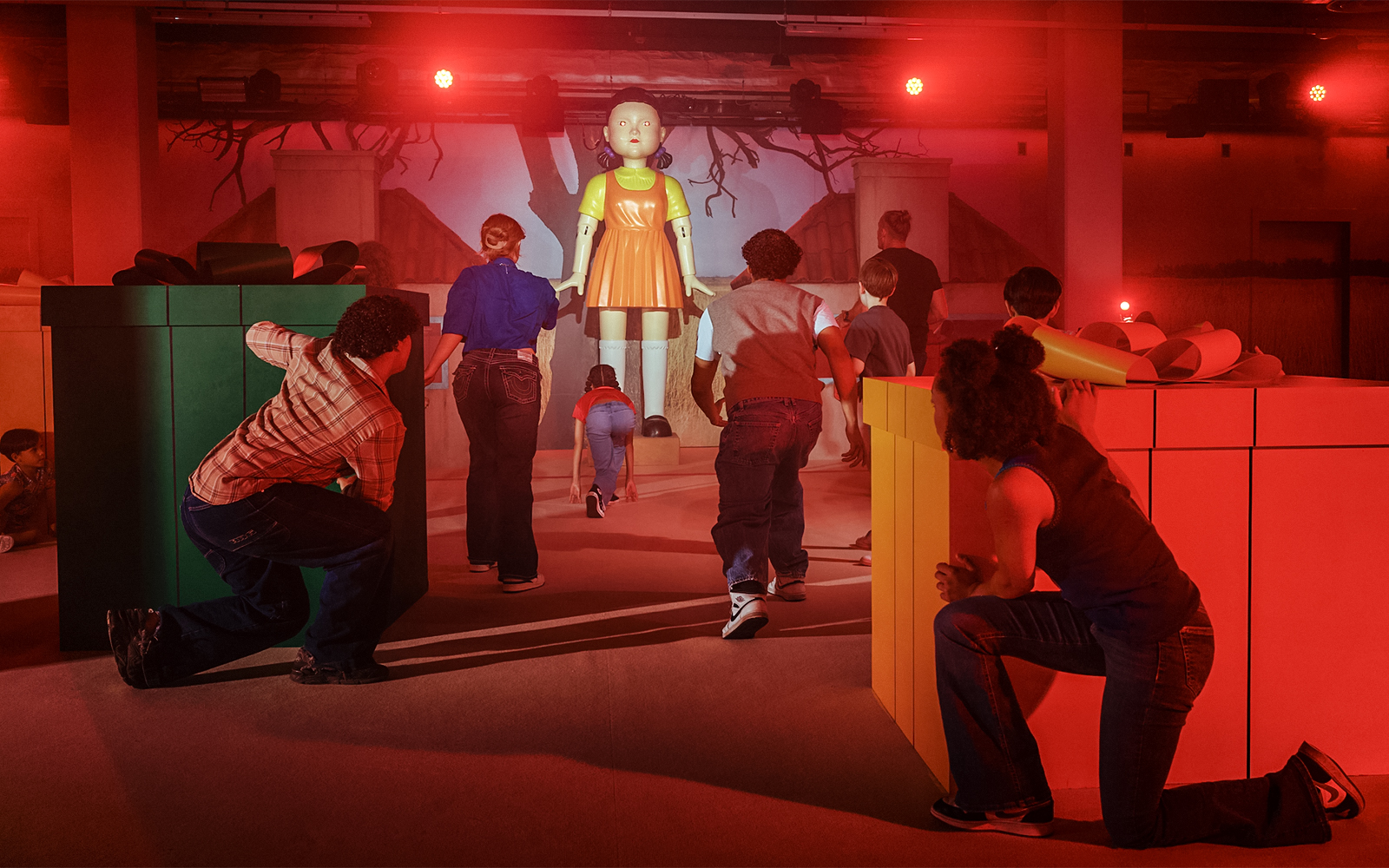 Participants in a Squid Game experience in London, hiding and moving towards a large doll.