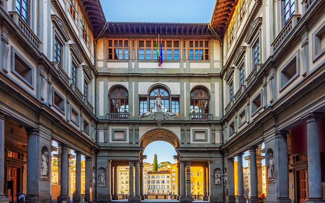 Sunlit corridor of Uffizi Gallery with arched openings framing Florence cityscape.