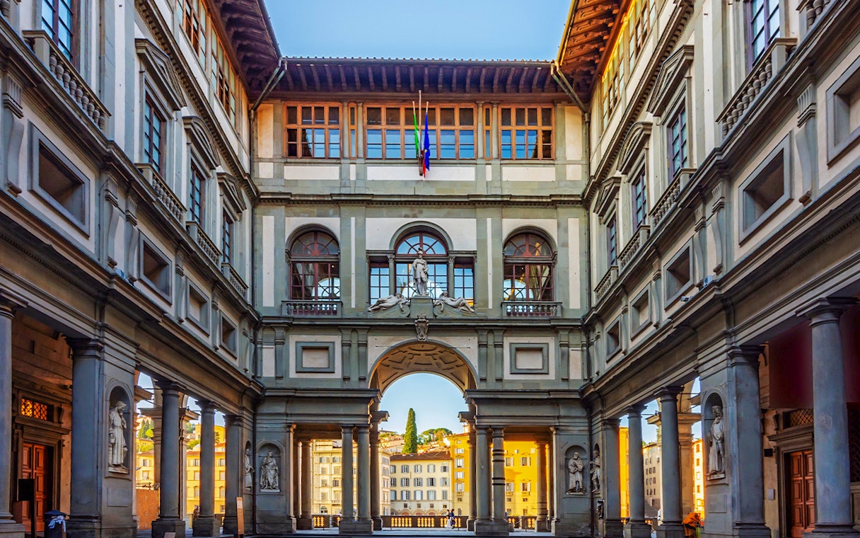 Sunlit corridor of Uffizi Gallery with arched openings framing Florence cityscape.