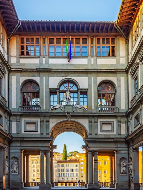 Sunlit corridor of Uffizi Gallery with arched openings framing Florence cityscape.