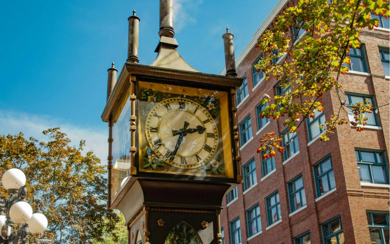 Gastown Steam Clock in Vancouver with nearby brick building and autumn trees.