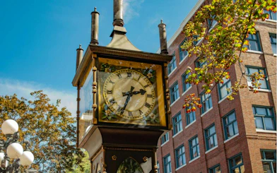 Gastown Steam Clock in Vancouver with nearby brick building and autumn trees.