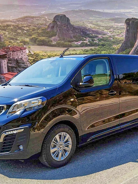 VIP van parked with Meteora rock formations in Greece in the background.