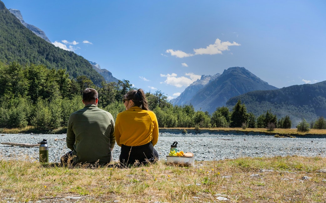 Couple enjoying a picnic by the Dart River with mountain views in New Zealand.