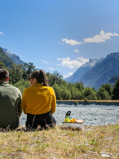 Couple enjoying a picnic by the Dart River with mountain views in New Zealand.