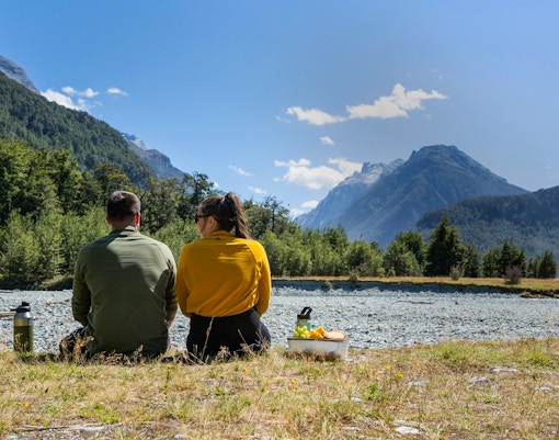 Couple enjoying a picnic by the Dart River with mountain views in New Zealand.