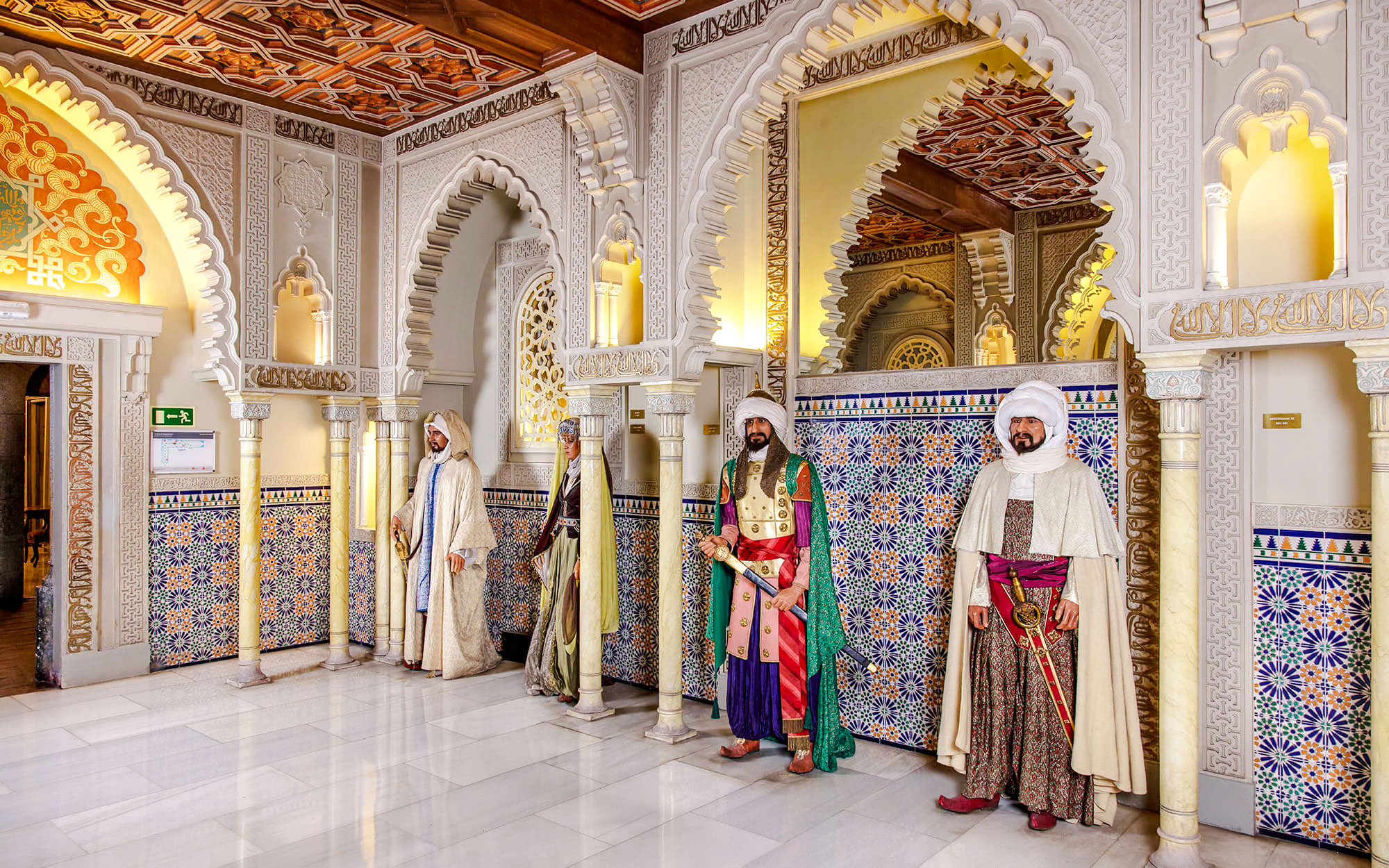 Wax figures in traditional attire at Museo de Cera, Madrid, with ornate arches and tile patterns.