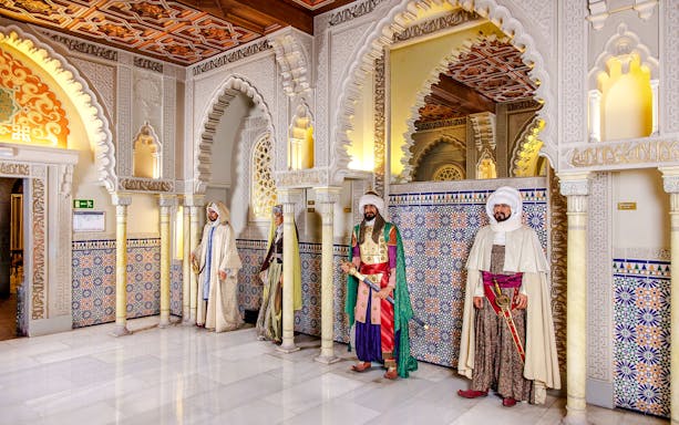Wax figures in traditional attire at Museo de Cera, Madrid, with ornate arches and tile patterns.