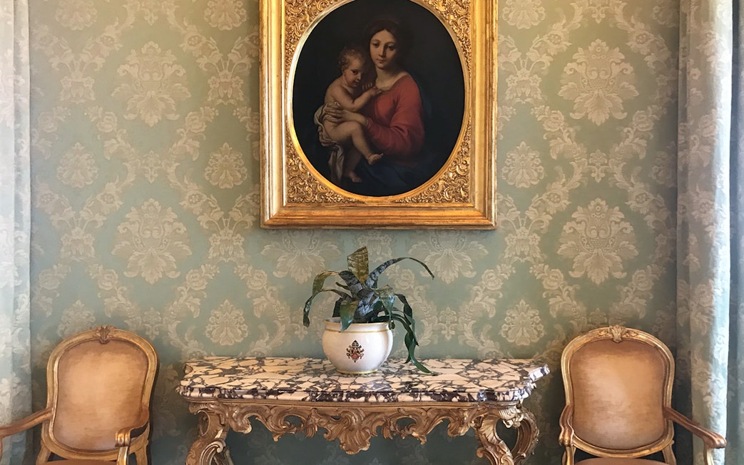 Painting and ornate table inside Castle Gandolfo with elegant chairs and wallpaper.