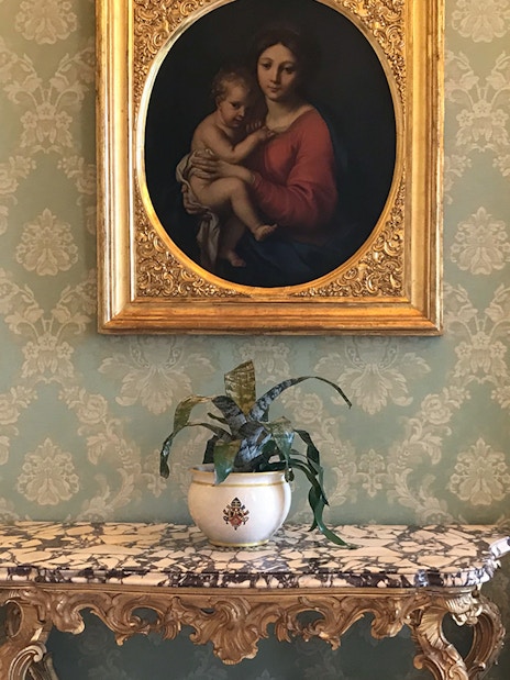 Painting and ornate table inside Castle Gandolfo with elegant chairs and wallpaper.