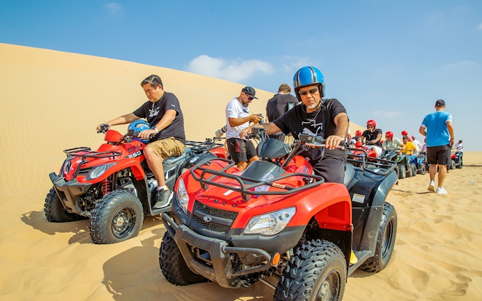 Quad bike riders on desert tour in Abu Dhabi sand dunes.