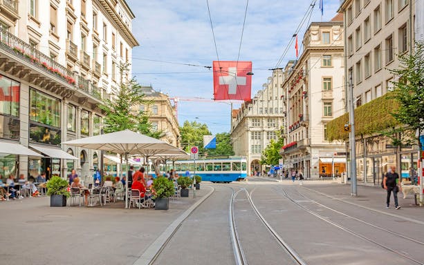 Zürich city street with tram, Swiss flag, and outdoor café.
