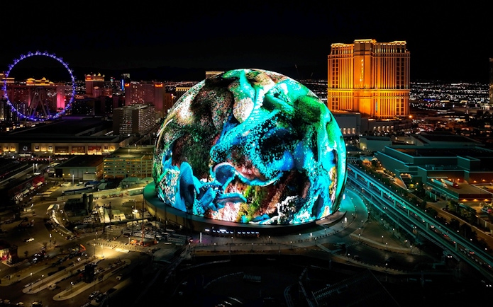 Las Vegas Sphere illuminated at night with vibrant display, Nevada skyline in background.