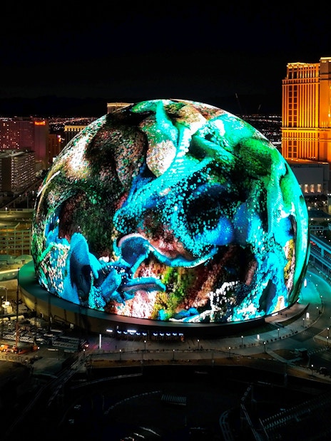 Las Vegas Sphere illuminated at night with vibrant display, Nevada skyline in background.