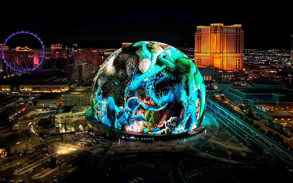 Las Vegas Sphere illuminated at night with vibrant display, Nevada skyline in background.
