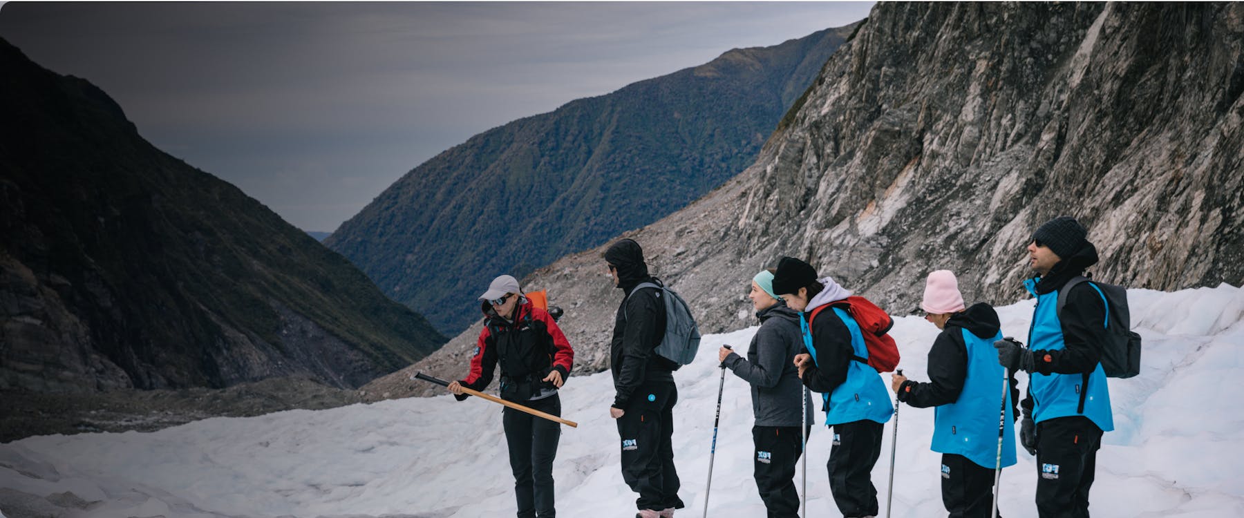 Group hiking on Fox Glacier, New Zealand, with guide explaining terrain.