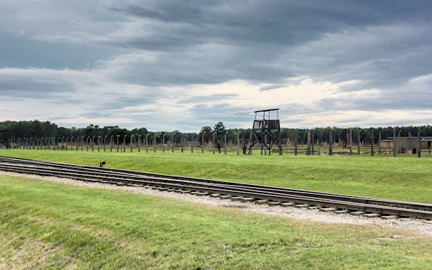 Rail tracks leading to Auschwitz with watchtower in the background, part of Krakow day tour.