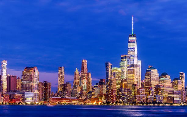 Manhattan skyline at dusk with illuminated skyscrapers.