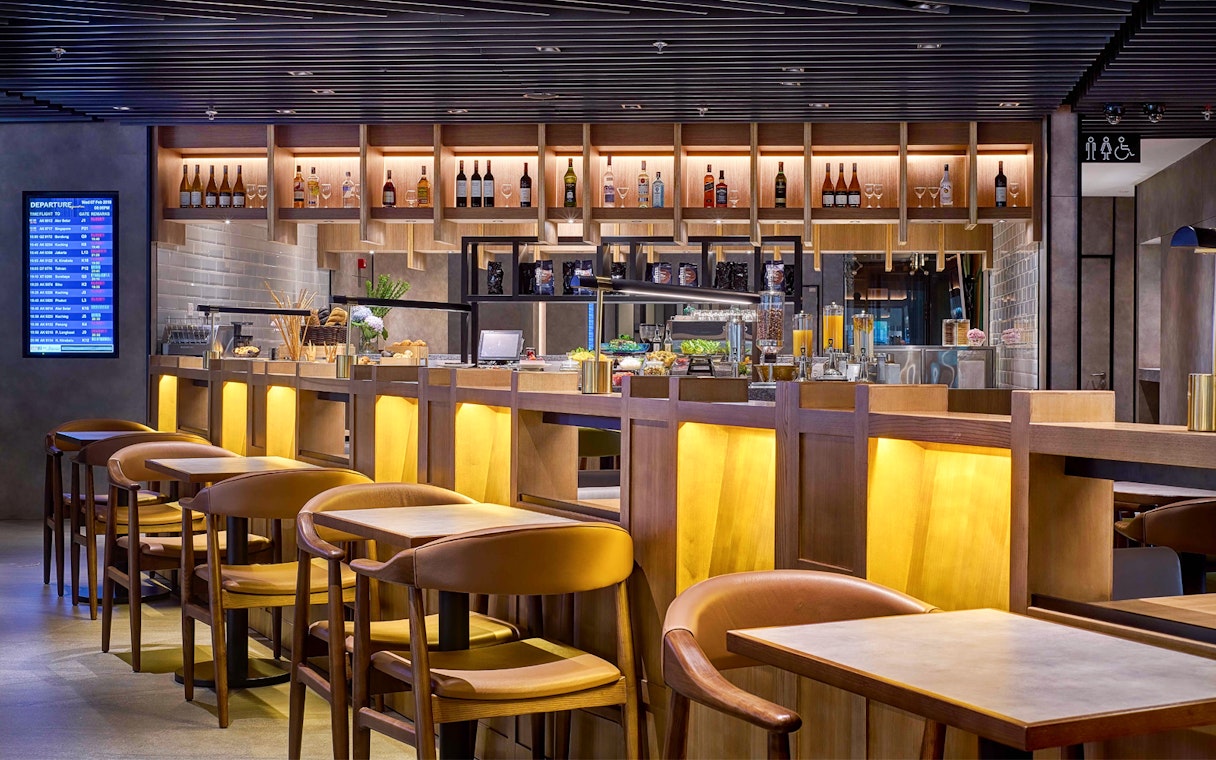 Plaza Premium Lounge seating and bar area at KLIA Terminal 2 with departure board.