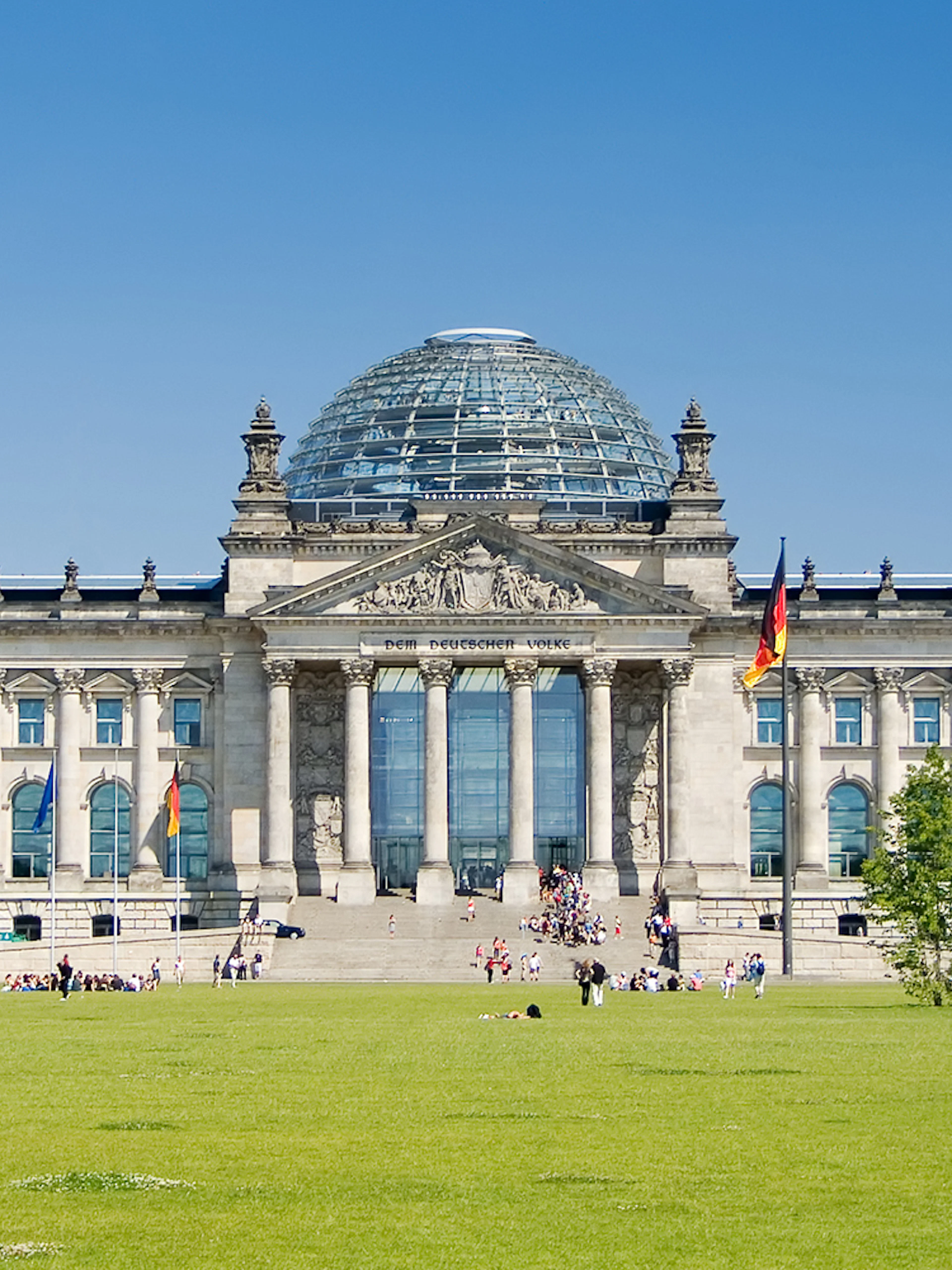 Reichstag building in Berlin with glass dome and German flags.