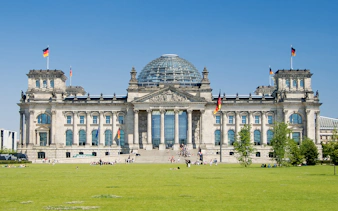 Reichstag building in Berlin with glass dome and German flags.