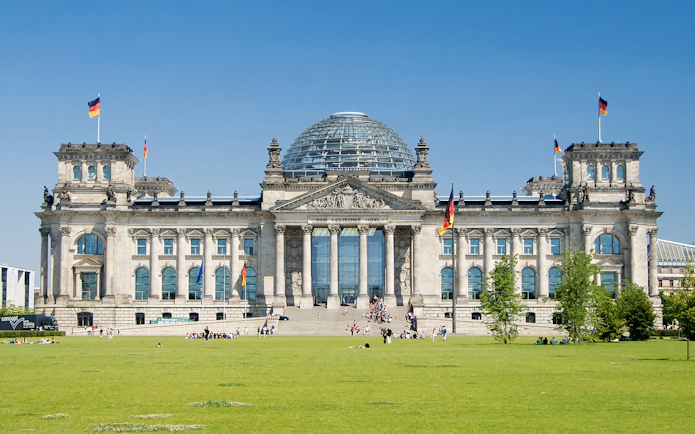 Reichstag building in Berlin with glass dome and German flags.