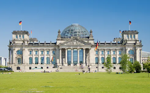 Reichstag building in Berlin with glass dome and German flags.