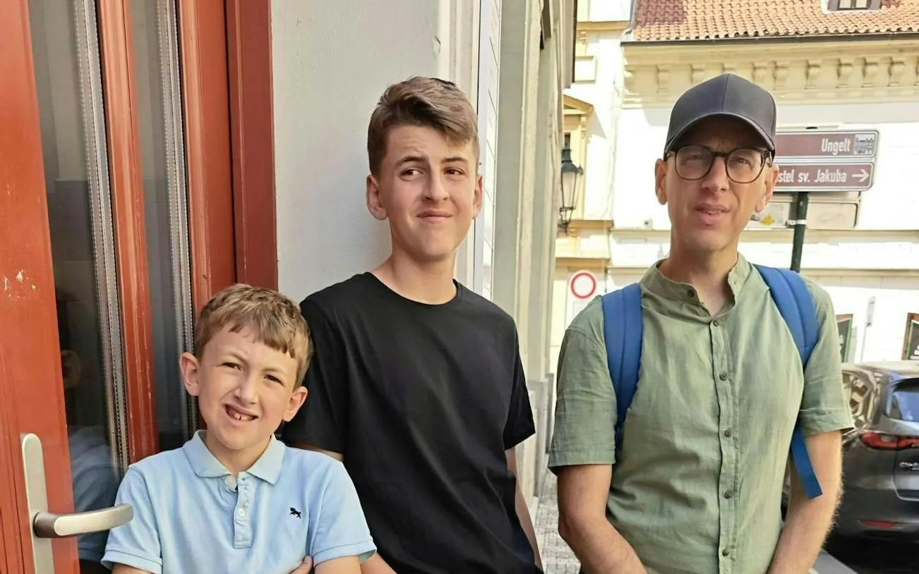 Three people standing on a street in Prague, near a sign for the Alchemy Mission city exploration game.