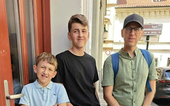 Three people standing on a street in Prague, near a sign for the Alchemy Mission city exploration game.