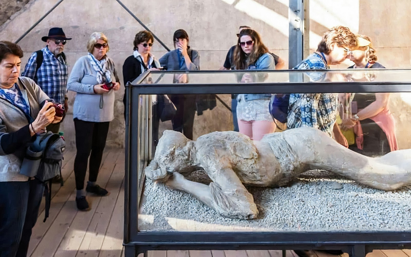 Visitors observing preserved volcanic victim in Pompeii, Italy.