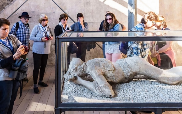 Visitors observing a plaster cast of a volcano victim in Pompeii.