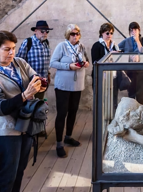Visitors observing a plaster cast of a volcano victim in Pompeii.