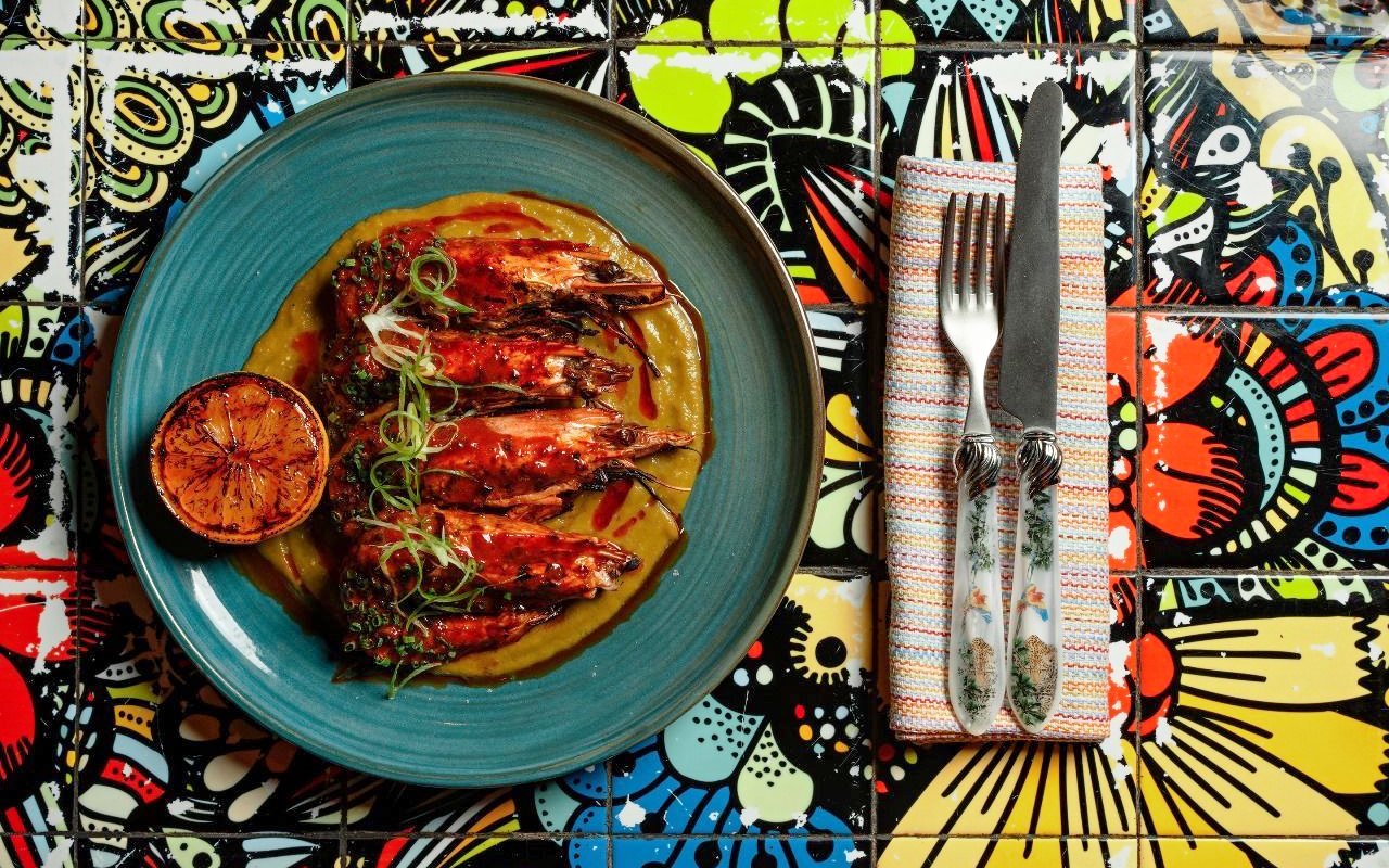 Grilled prawns with sauce and charred lemon on a colorful table at En Fuego Fiesta Mexicana Brunch, Dubai.