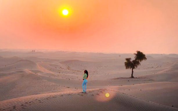 Person standing on sand dune during sunrise in Abu Dhabi desert.