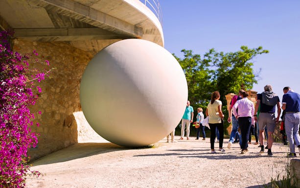 Visitors exploring a winery in Barcelona with a large spherical sculpture.