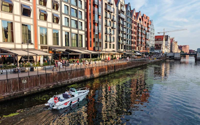 Electric boat on Gdansk harbour during Motława Sunset Cruise with waterfront buildings.