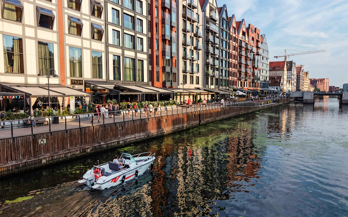 Electric boat on Gdansk harbour during Motława Sunset Cruise with waterfront buildings.