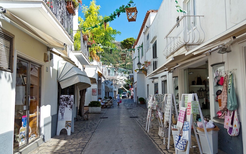 Narrow street in Capri lined with shops and outdoor displays, showcasing local charm.