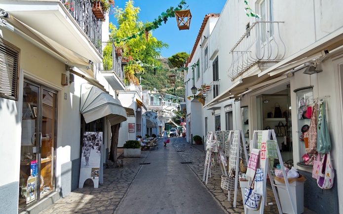 Narrow street in Capri lined with shops and outdoor displays, showcasing local charm.