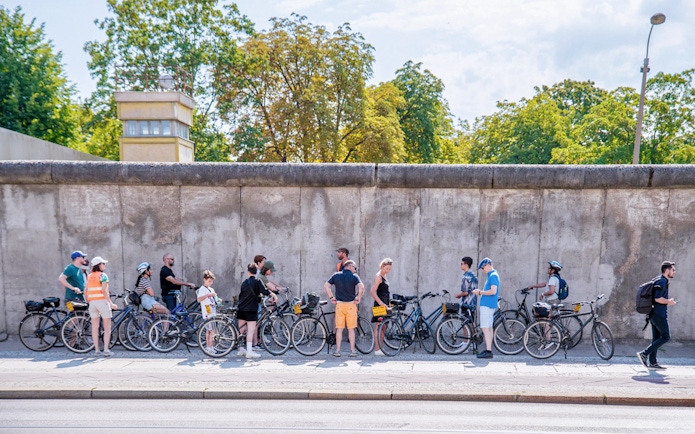 Cyclists on a guided tour stop at the Berlin Wall, Berlin.