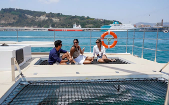 Tourists relaxing on an eco catamaran cruise in Barcelona with scenic coastline views.