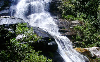 Waterfall cascading over rocks in Tijuca Forest, Rio de Janeiro, surrounded by lush greenery.