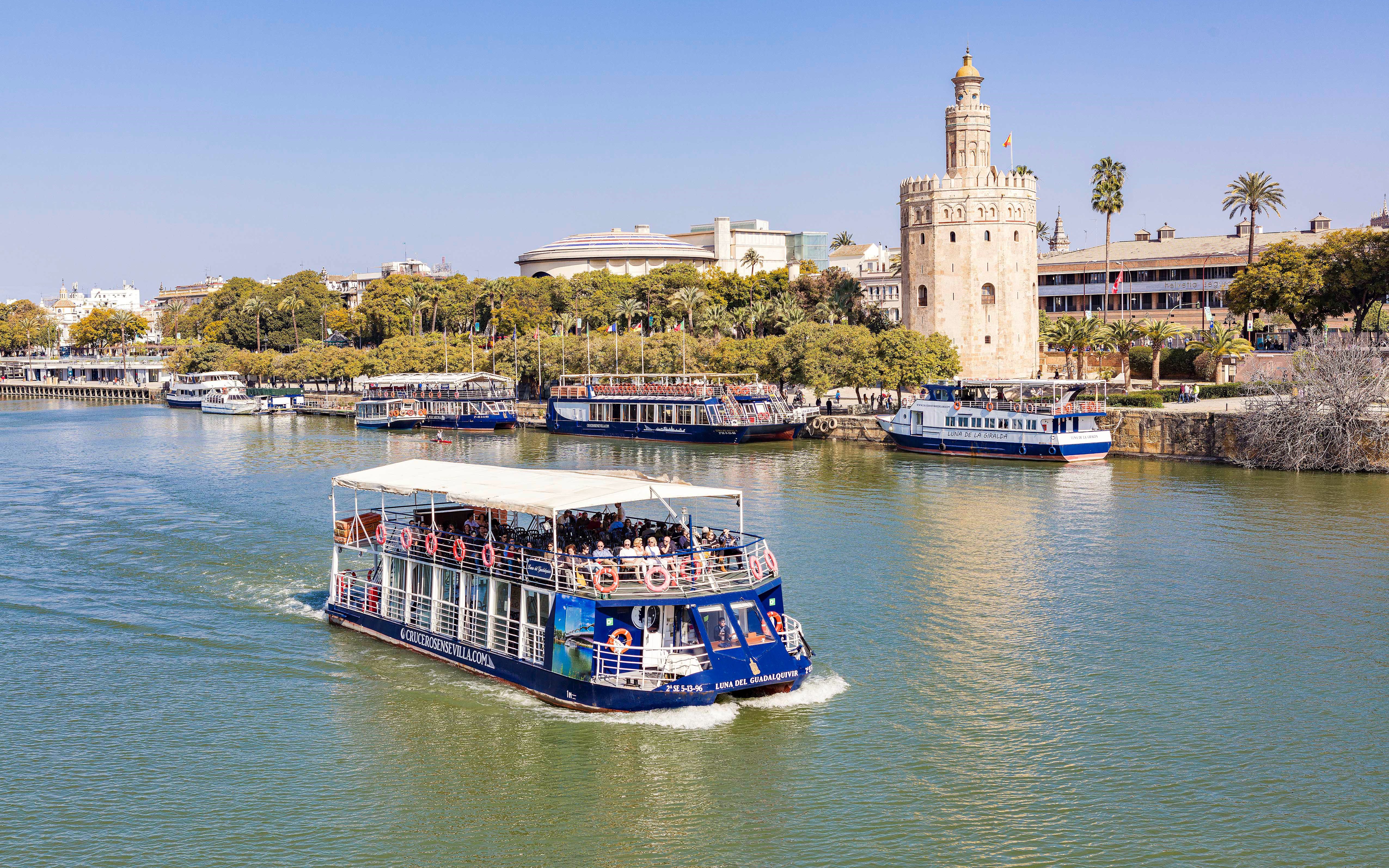 Cruise boat on Guadalquivir River passing Torre del Oro in Seville.