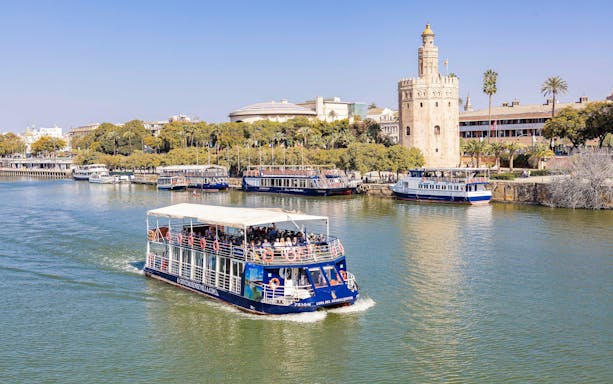 Cruise boat on Guadalquivir River passing Torre del Oro in Seville.